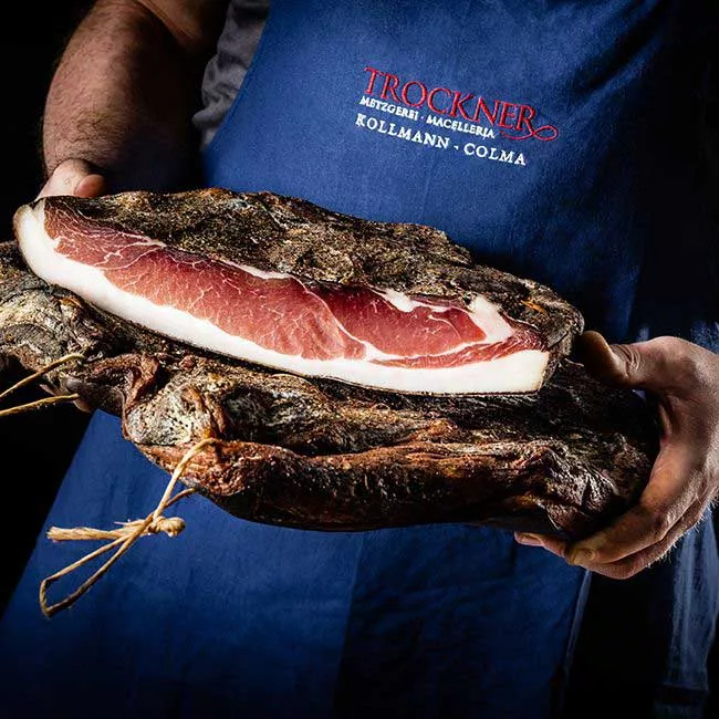 Metzger mit blauem Schurz und halben Speck in den Händen