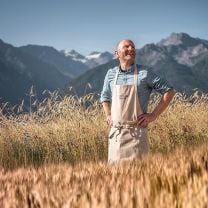 Tradition trifft Natur: Hannes Schwienbacher, Bäcker von Ultner Brot im Südtiroler Kornfeld mit Blick auf die Alpen.